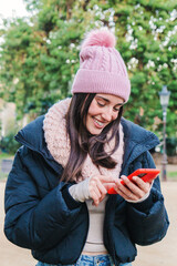 Vertical portrait of a caucasian woman smiling typing with a cell phone in a social media app. Front view of a teenage girl using a smartphone for send messages to her friends. Communication concept