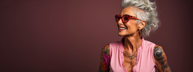 Radiant elderly lady with white hair revealing bold chest tattoo, her warm smile exuding joy and confidence against a plain studio background.