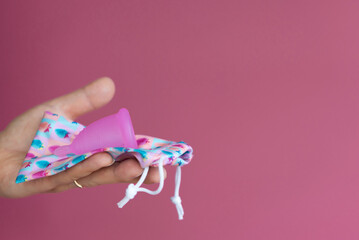 Reusable menstrual cup in a woman's hand on a delicate pink background. Method of storing the menstrual cup. Сoncept female intimate hygiene period products and zero waste. Minimalism. Copyspace.
