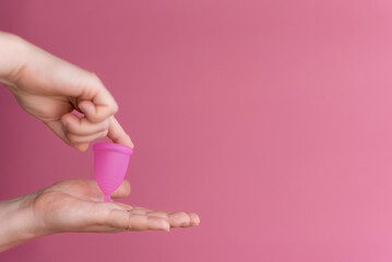 Reusable menstrual cup in the hands of a woman on a delicate pink background. Сoncept female intimate hygiene period products and zero waste. Minimalism. Copyspace.