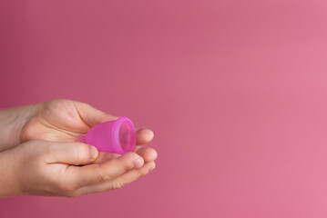Reusable menstrual cup in the hands of a woman on a delicate pink background. Сoncept female...