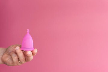 Reusable menstrual cup in a woman's hand on a delicate pink background. Сoncept female intimate hygiene period products and zero waste. Minimalism. Copyspace.