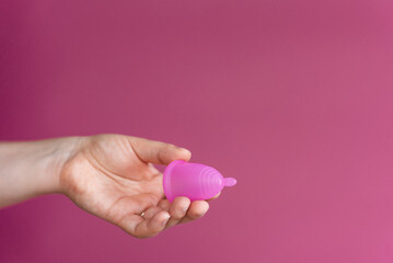 Reusable menstrual cup in a woman's hand on a delicate pink background. Сoncept female intimate hygiene period products and zero waste. Minimalism. Copyspace.