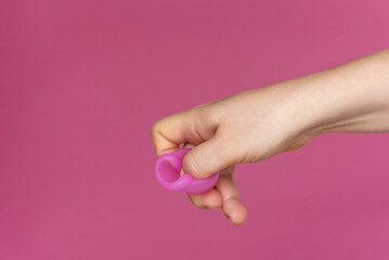Reusable menstrual cup in the hands of a woman on a delicate pink background. How to fold the menstrual cup. Сoncept female intimate hygiene period products and zero waste. Minimalism. Copyspace.