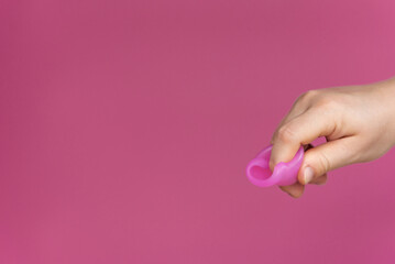 Reusable menstrual cup in the hands of a woman on a delicate pink background. How to fold the menstrual cup. Сoncept female intimate hygiene period products and zero waste. Minimalism. Copyspace.