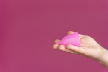 Reusable menstrual cup in a woman's hand on a delicate pink background. Сoncept female intimate hygiene period products and zero waste. Minimalism. Copyspace.