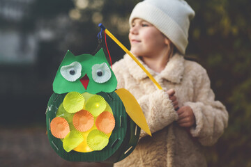Little preschool kid girl holding selfmade traditional owl lanterns with candle for St. Martin...