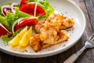 Seared cod loin and fresh vegetables on wooden table
