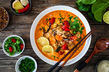 Tom Yum soup - Thai soup with chicken breast nuggets and noodles on wooden table
