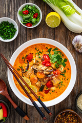 Tom Yum soup - Thai soup with chicken breast nuggets and noodles on wooden table

