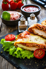 Fototapeta na wymiar Milanesa Napolitana - fried breaded cutlet with ham, mozzarella cheese and tomato sauce on wooden background 