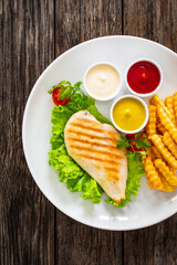 Grilled chicken breast, French fries and fresh vegetables on wooden table
