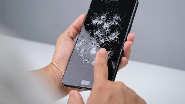 Female hand holding a smartphone with a broken screen and touching the screen isolated on white background. Smartphone damage, touch screen scratched with spider web.