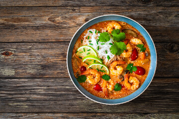 Tom Yum soup - Thai soup with prawns and rice noodles on wooden table


