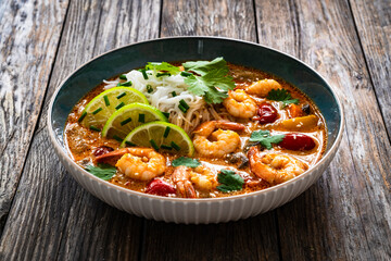 Tom Yum soup - Thai soup with prawns and rice noodles on wooden table

