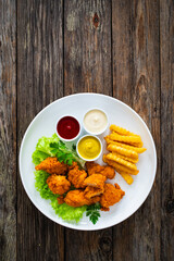 Seared breaded chicken nuggets with French fries on wooden table
