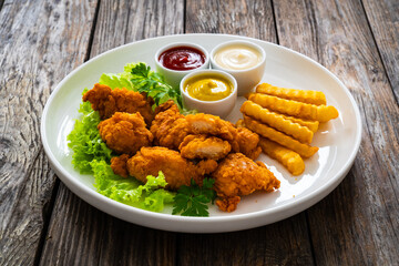 Seared breaded chicken nuggets with French fries on wooden table
