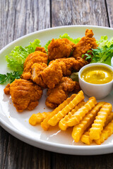 Seared breaded chicken nuggets with French fries on wooden table
