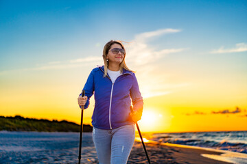 Nordic walking - woman exercising on beach at sunset
