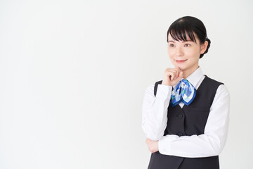 顎に手を当てるベストにリボンタイの制服を着た、受付業務、事務業務の女性