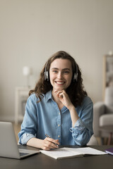 Cheerful gen Z online student girl in headphones studying at home, sitting at laptop, using...