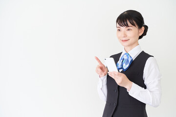 スマートフォンを操作するベストにリボンタイの制服を着た、受付業務、事務業務の女性