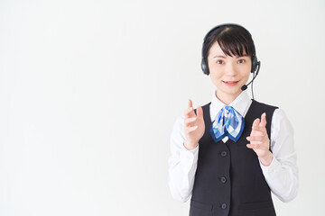 ヘッドセットをするベストにリボンタイの制服を着た、受付業務、事務業務の女性