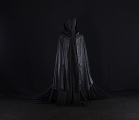 Naklejka premium witch in a black cloak on a black background