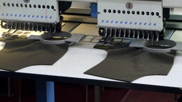 Sewing machine for automatic embroidery in work. Close-up of a line of embroidery logos on the fabric. Sewing factory, textile production.	