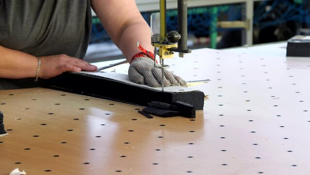 A woman sewing worker cuts excess fabric according to patterns with a special saw. Working with a jigsaw wearing protective metal gloves. Industrial safety. Sewing factory, textile production.