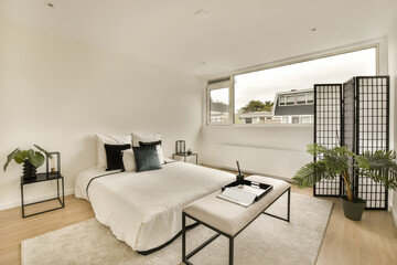 a bedroom with white walls and wood flooring in the room, there is a large window that looks out onto the street