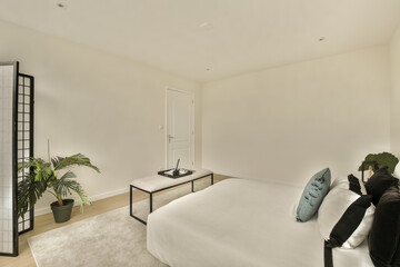 a bedroom with a white bed and some green plants in the photo is taken from the other side of the room