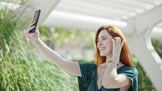 Young redhead woman smiling confident making selfie by the smartphone at park