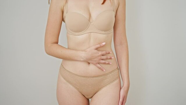 Young redhead woman wearing lingerie massaging belly over isolated white background