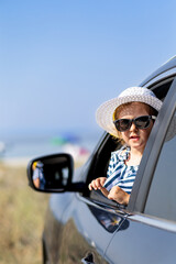 Fashionable happy kid girl, peeks out of the car in the sunset. Beach and sea in the background. Travel summer vacation concept.