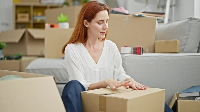 Young redhead woman packing cardboard box at new home