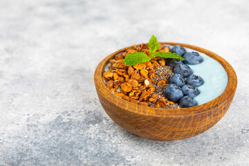Bowl of granola with yogurt and fresh berries on a texture table. Yogurt berries, acai bowl, spirulina bowl. Healthy food, balanced breakfast. Strawberries, blueberries, kiwi, peach, almonds and chia.