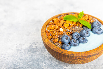 Bowl of granola with yogurt and fresh berries on a texture table. Yogurt berries, acai bowl, spirulina bowl. Healthy food, balanced breakfast. Strawberries, blueberries, kiwi, peach, almonds and chia.