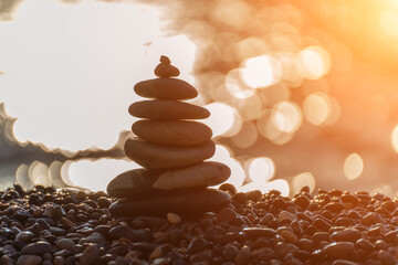 Balanced rock pyramid on pebbles beach. Golden sea bokeh on background. Selective focus, zen stones on sea beach, meditation, spa, harmony, calm, balance concept.