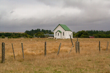 White wooden building with a green roof in a rural farming field. Martinborough, New Zealand.