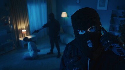 Shot of two burglars holding a young woman hostage. One of them is pointing a gun at the victim,...