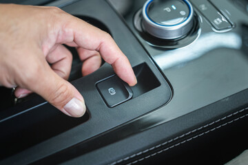 Action of a car driver is using finger to activate the eletrical parking brake system by pulling the button. Transporation equipment object photo, selective focus.
