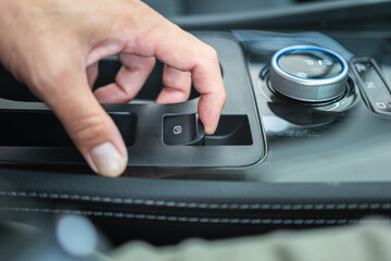 Action of a car driver is using finger to activate the eletrical parking brake system by pulling the button. Transporation equipment object photo, selective focus.