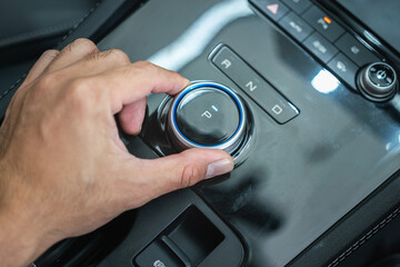 Action of the car driver is shifting the electrical gear to Parking position. Close-uo and selective focus.