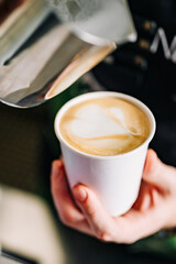Professional barista hands pouring steamed milk into coffee paper cup making coffee.
