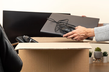 Woman hands put old laptop computer in cardboard box with old used tech gadget devices for...