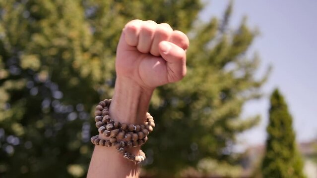 A close-up of a man's fist raised up with bracelets on his wrist gesticulates protest and disagreement with the violation of people's rights. Against discrimination on racial and sexual grounds