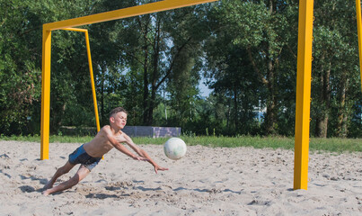 A little boy is playing soccer on the sand