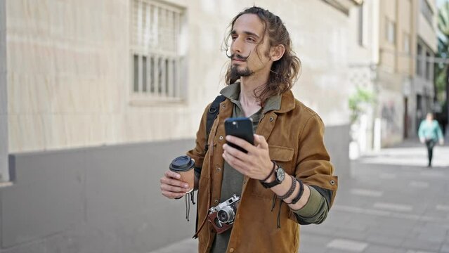 Young hispanic man tourist using smartphone holding coffee at street