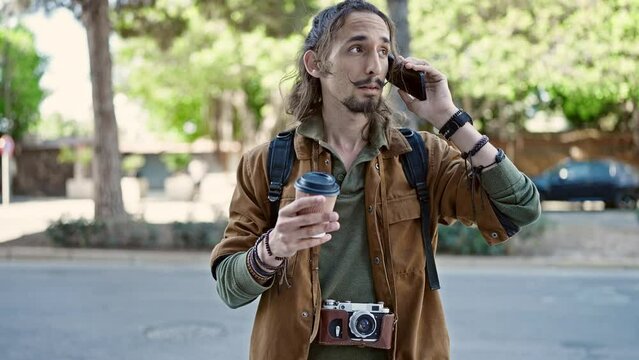 Young hispanic man tourist talking on smartphone holding coffee at park